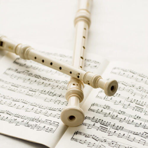 Two block-flutes placed over textbook with musical notes. High key